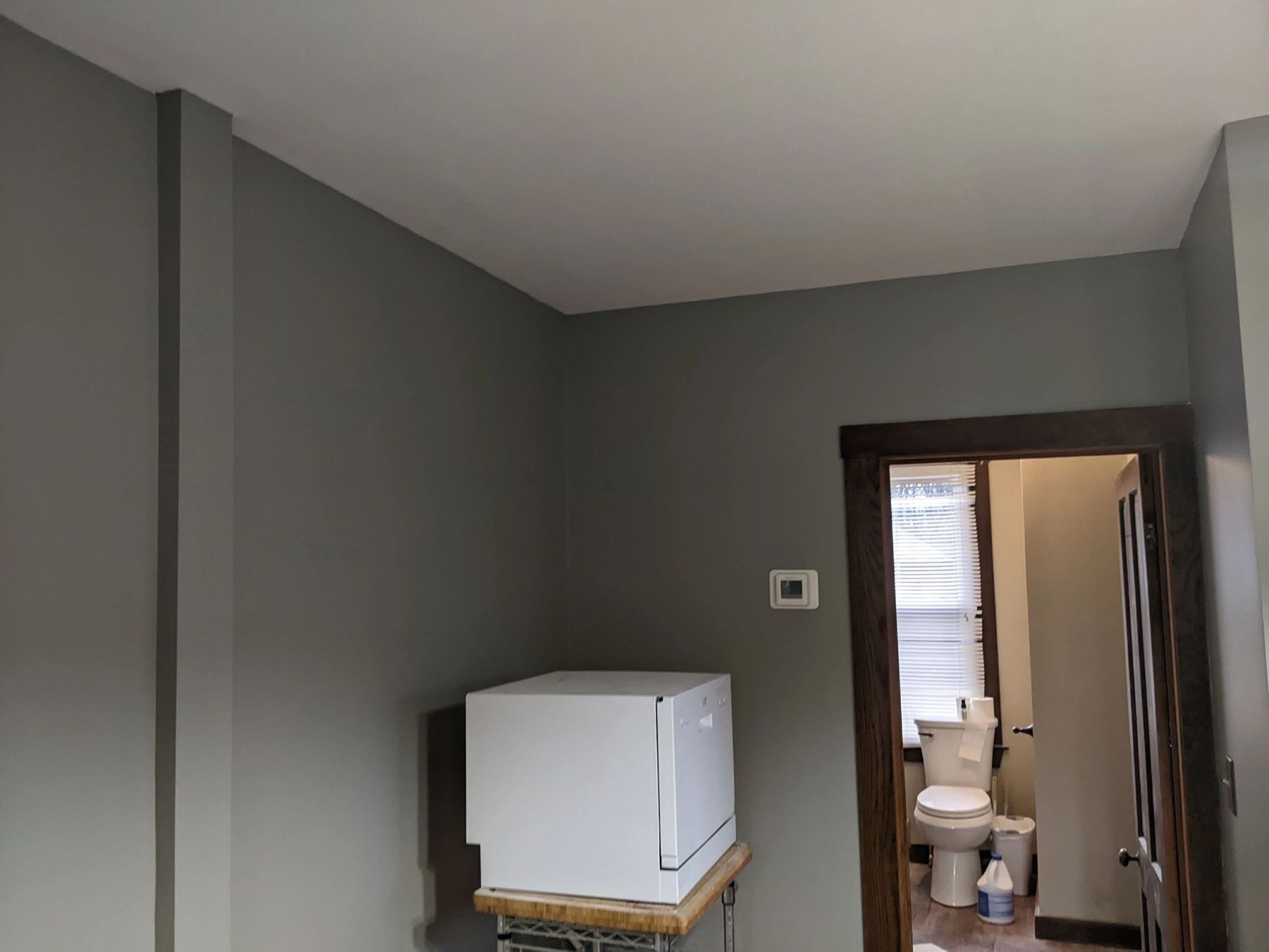 Freshly painted grey room with a new dark-stained door casing leading to a bathroom