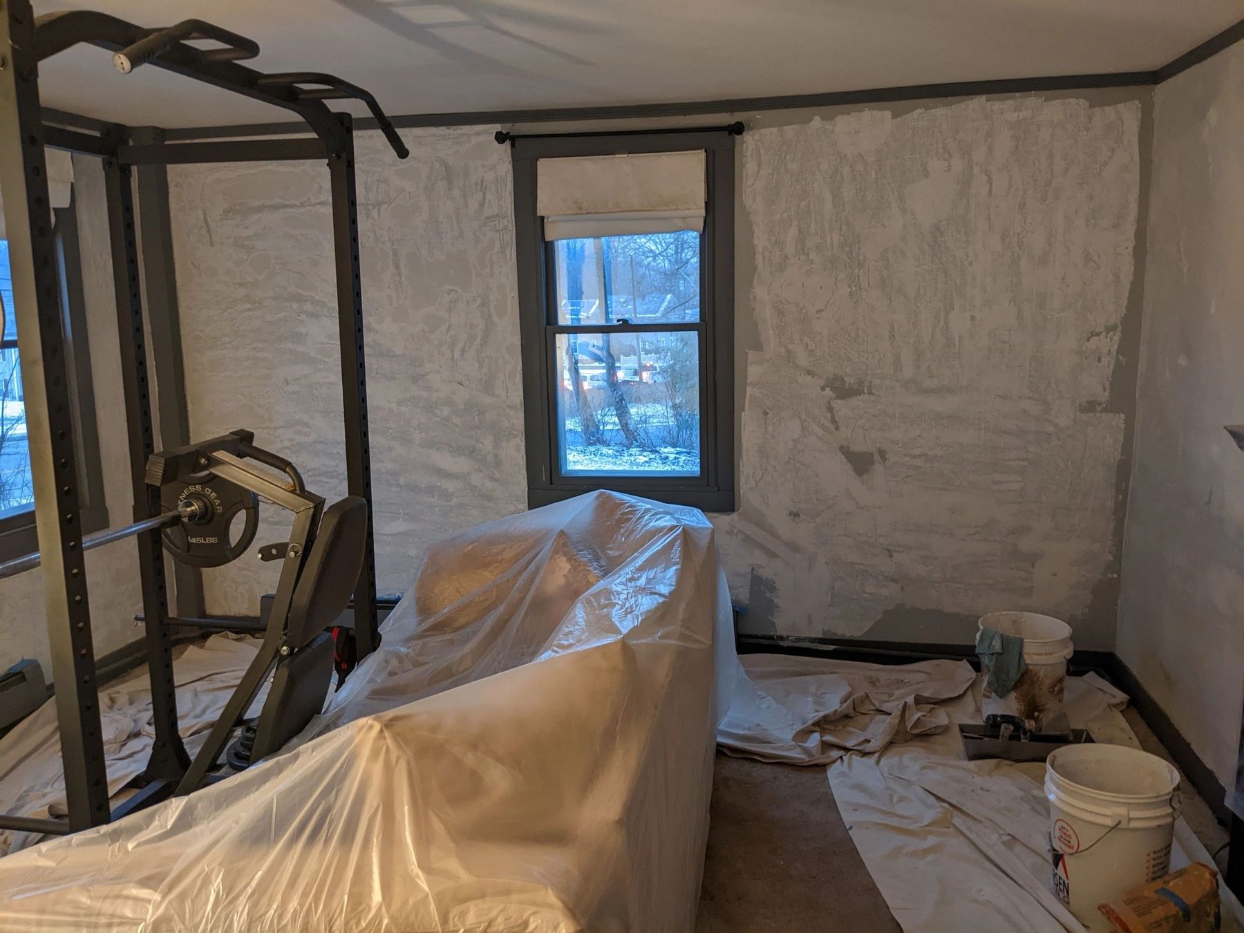 Room prepped for repair with furniture covered in plastic and walls primed